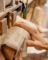 Close-up of hands shaping a light-colored leather boot on a wooden mold using a machine in a workshop.