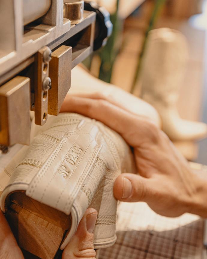 Close-up of hands shaping a light-colored leather boot on a wooden mold using a machine in a workshop.