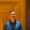 A man in a blue shirt standing in front of a wooden door.