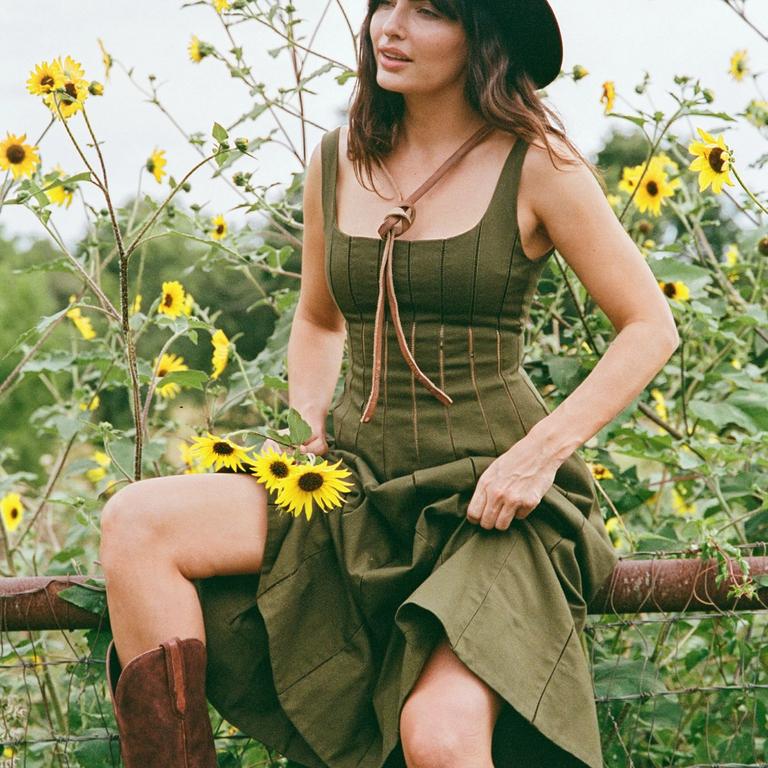 a woman in a field on a farm fence wearing a green dress and red cowgirl boots