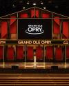 Empty stage at the Grand Ole Opry with a microphone stand in front, red and black backdrop, and "Grand Ole Opry" displayed on a screen.