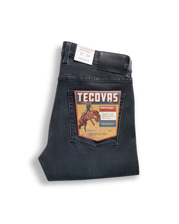 Folded pair of dark wash Tecovas jeans with a retail label featuring a rider on a horse, displayed on the back pocket.