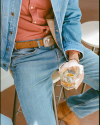 A person dressed in denim jeans and a denim jacket sits on a stool holding a glass of light-colored beverage.