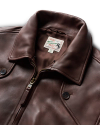 Close-up photo of a brown leather jacket with a visible label on the collar reading "Rough Riders Tooled Leather." The jacket features a zipper and large buttons.