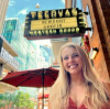 A person smiles in front of a storefront with a sign reading "Tecovas Newboot Goofin Western Goods." Buildings and an umbrella are visible in the background.