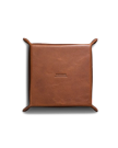 A square brown leather valet tray with raised corners and "TROGURS" embossed in the center, placed on a white background.