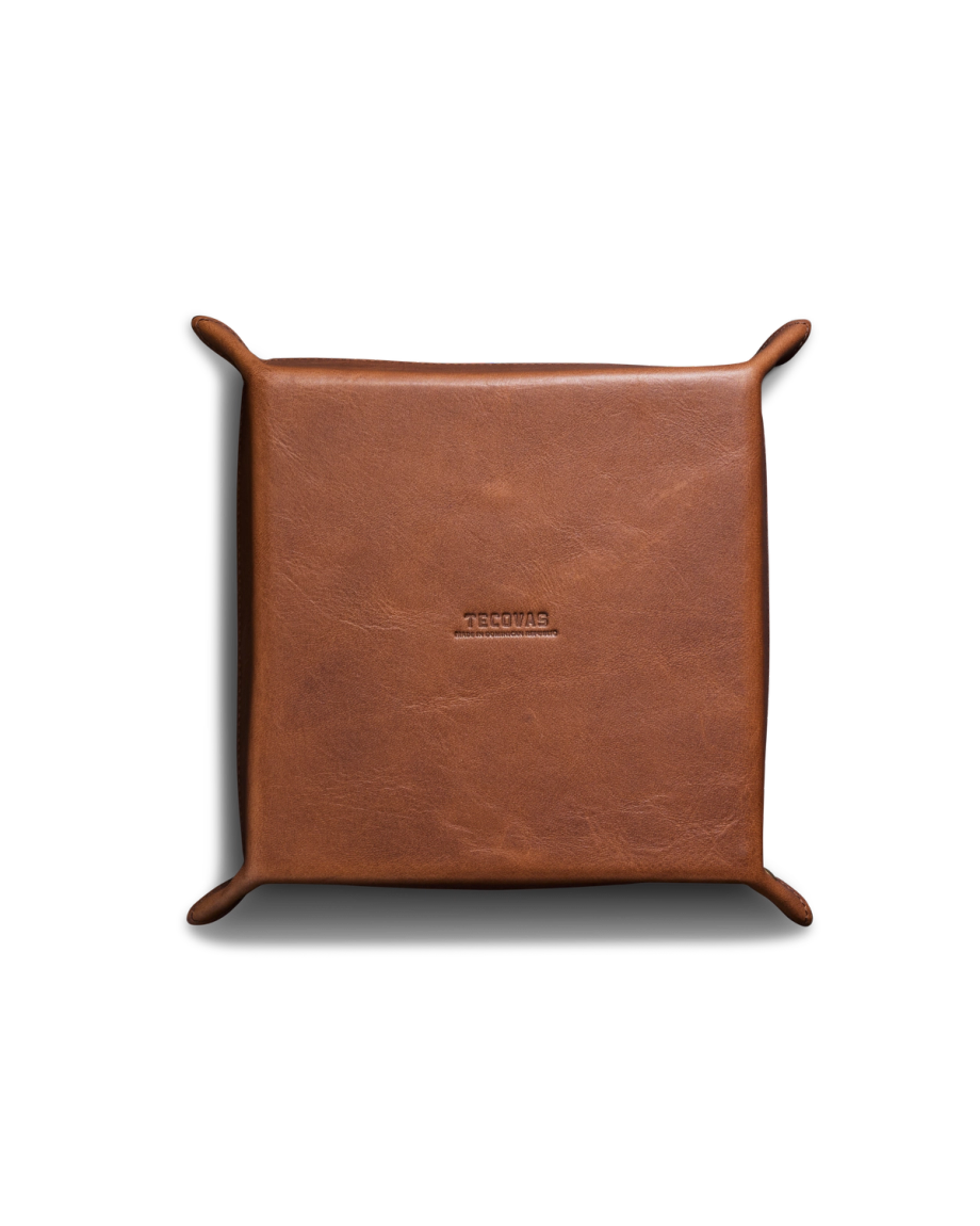 A square brown leather valet tray with raised corners and "TROGURS" embossed in the center, placed on a white background.