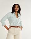 Person wearing a light blue button-up shirt, beige pants, and a brown belt, standing against a plain background.