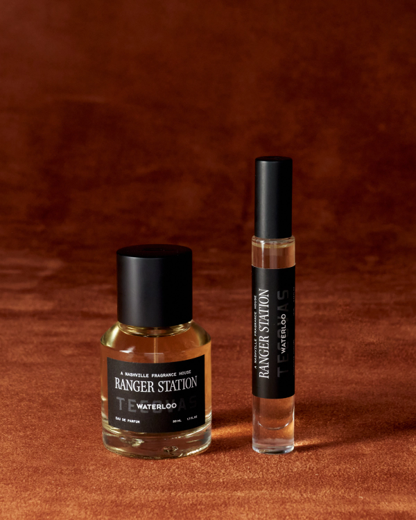 A bottle and a rollerball of Ranger Station Waterloo Eau de Parfum are placed on a brown textured surface.