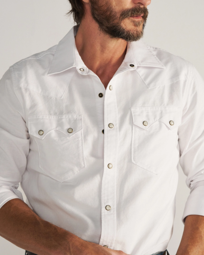 Man wearing a white long-sleeve button-up shirt with two front pockets, standing against a plain background.