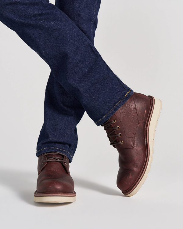 The Knox Lace Up in Cognac Cowhide. A person wearing dark blue jeans and cognac cowhide leather lace-up boots with light-colored soles.