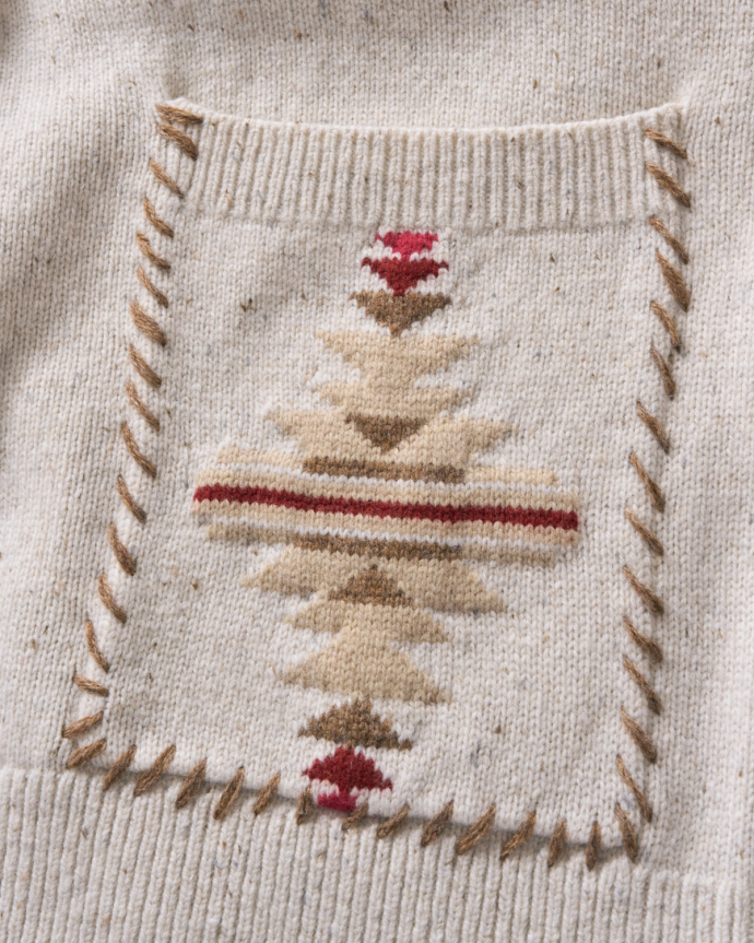 Close-up of a cream-colored knitted fabric with a square patch featuring a geometric design in brown, beige, and red.