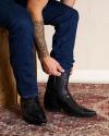 Man putting on the Tecovas Garrett snip toe boots in the color midnight ostrich. 