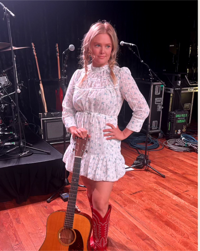 A woman in a white dress holding an acoustic guitar.