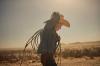 A child in a cowboy hat and denim shirt holds a coiled rope against a hazy desert backdrop.