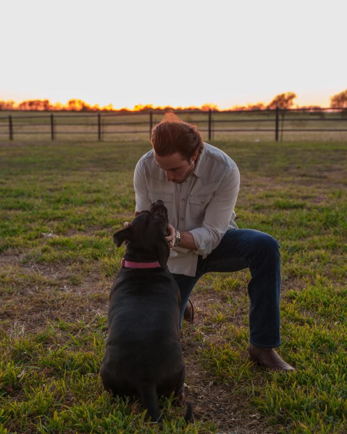 Man petting dog kneeling in grass