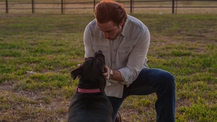 Man petting dog kneeling in grass