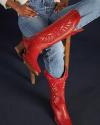 A person wearing blue jeans and red cowboy boots sits with one leg crossed over the other on a wooden chair against a dark background.