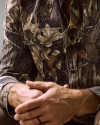 Close-up of a person wearing a camouflage-patterned shirt with “Tecovas” on the pocket, hands clasped in front.