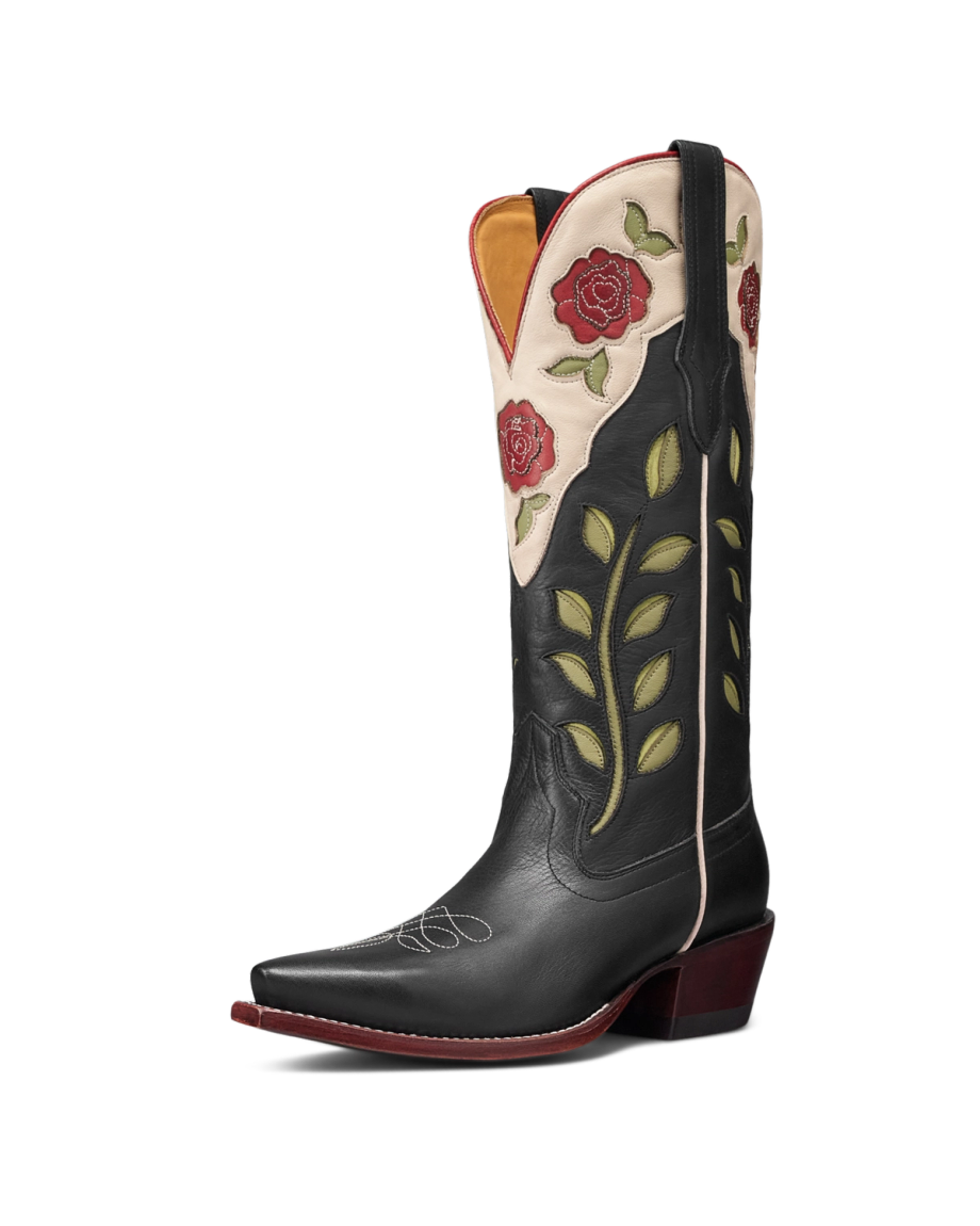 The Annie in Midnight Roses Cowhide. A black leather cowboy boot, known as the Midnight Roses Cowhide, features striking red rose and green leaf embroidery, white stitching on the toe, and a pointed toe with a stacked heel.