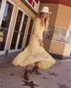 Person in a wide-brimmed hat and long yellow dress walking on a sidewalk with star-shaped decorations.