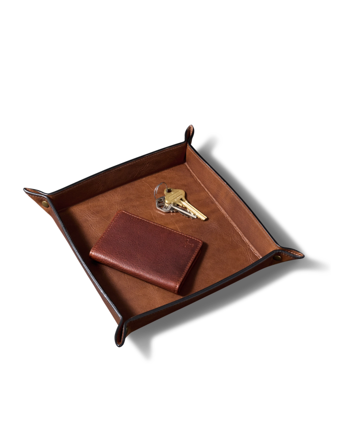 A brown leather valet tray containing a leather wallet and two metal keys on a white background.