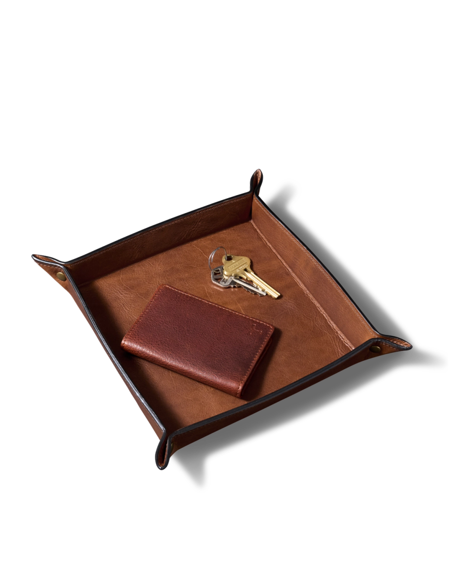 A brown leather valet tray containing a leather wallet and two metal keys on a white background.