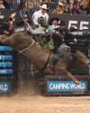 A bull rider grips a bucking bull in an arena, surrounded by officials, spectators, and large event signage.