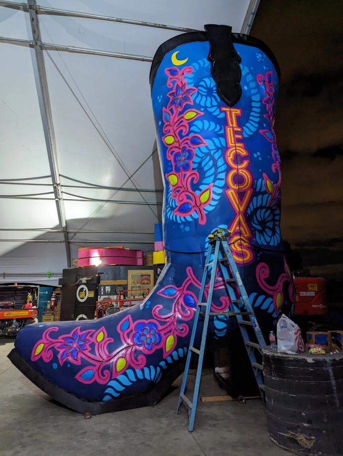 A large boot adorned with colorful floral patterns and a crescent moon, undergoing maintenance in a tented area at night.