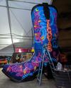 A large boot adorned with colorful floral patterns and a crescent moon, undergoing maintenance in a tented area at night.