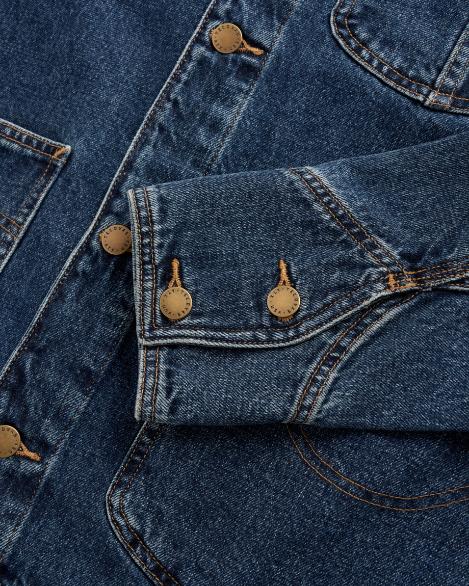 Close-up of a blue denim jacket showing a sleeve with three metal buttons and visible stitching.