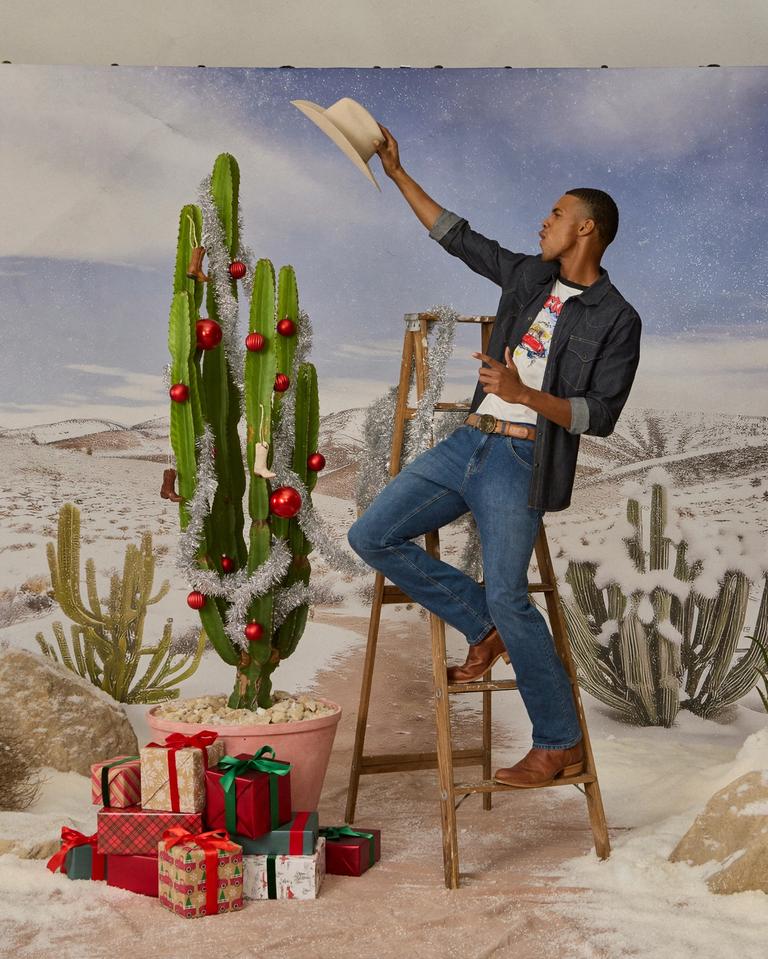 Man putting a cowboy hat on a cactus tree adorned with Christmas ornaments