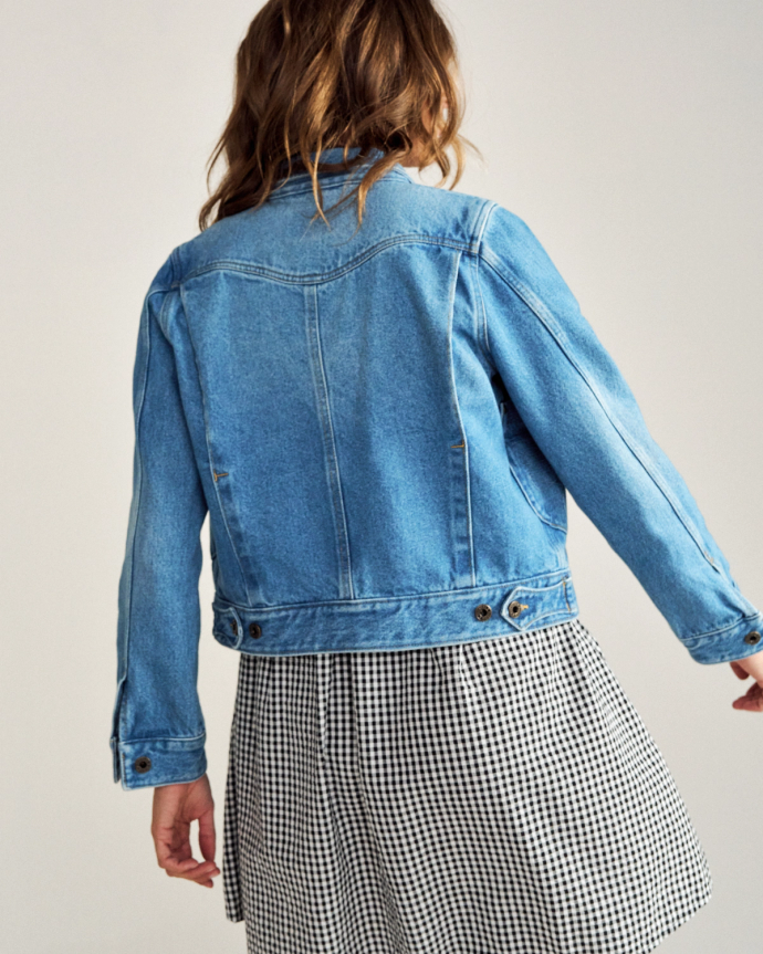 A person with wavy brown hair is shown from the back, wearing a blue denim jacket and a black-and-white checkered skirt.