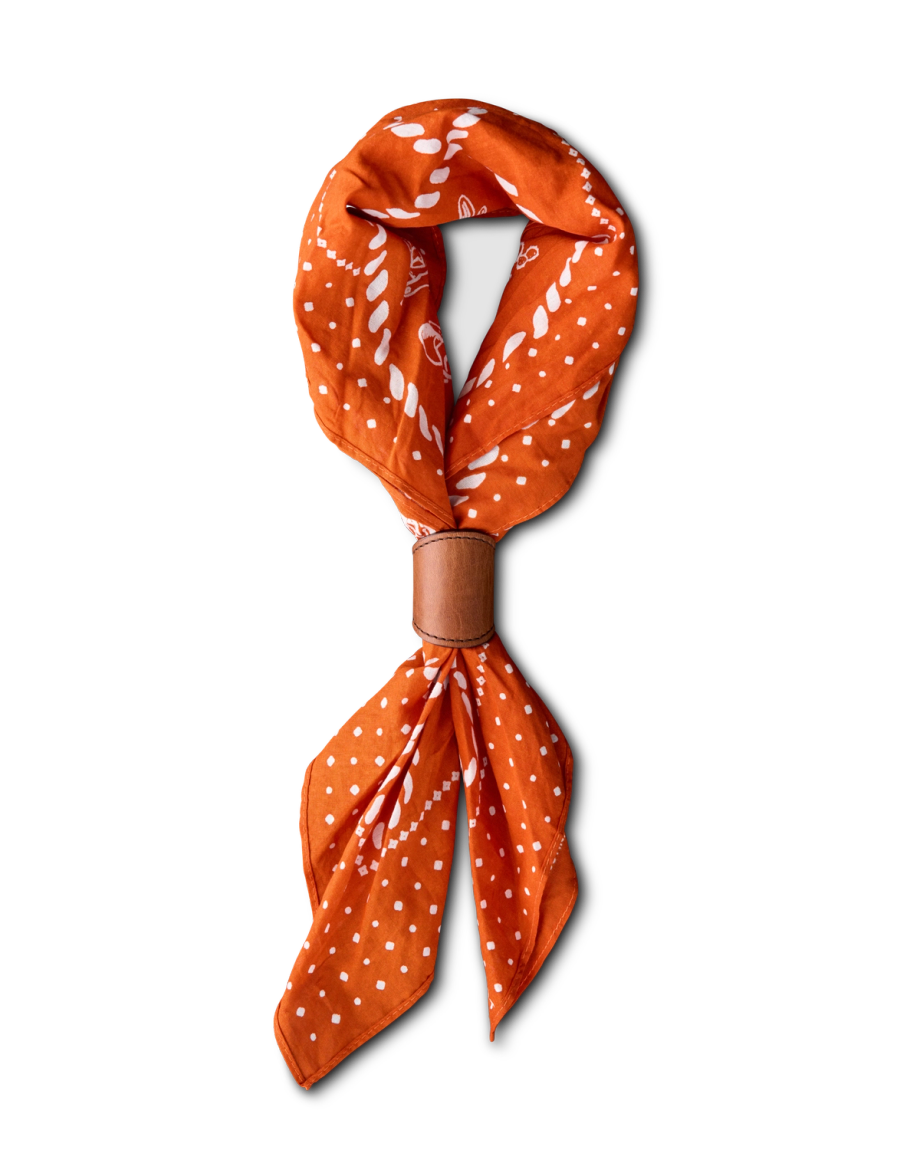 An orange bandana with white patterns, folded and held together by a brown leather band, displayed on a plain light background.