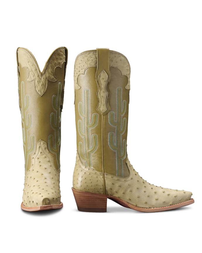 Two cowboy boots made of light-colored ostrich leather with tall shafts, cactus embroidery, and wooden heels, displayed against a black background.