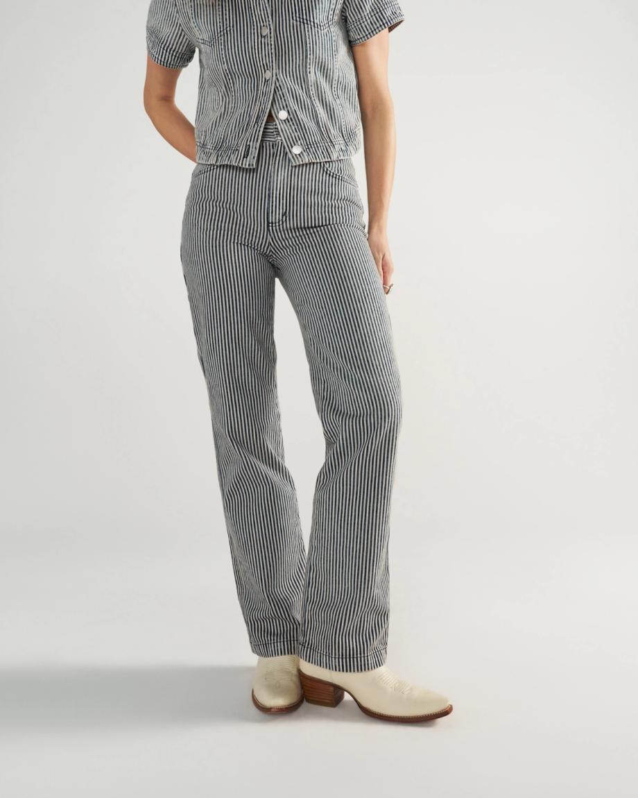 Person wearing a short-sleeve, button-up shirt and matching striped pants with white heeled shoes, standing against a plain background.