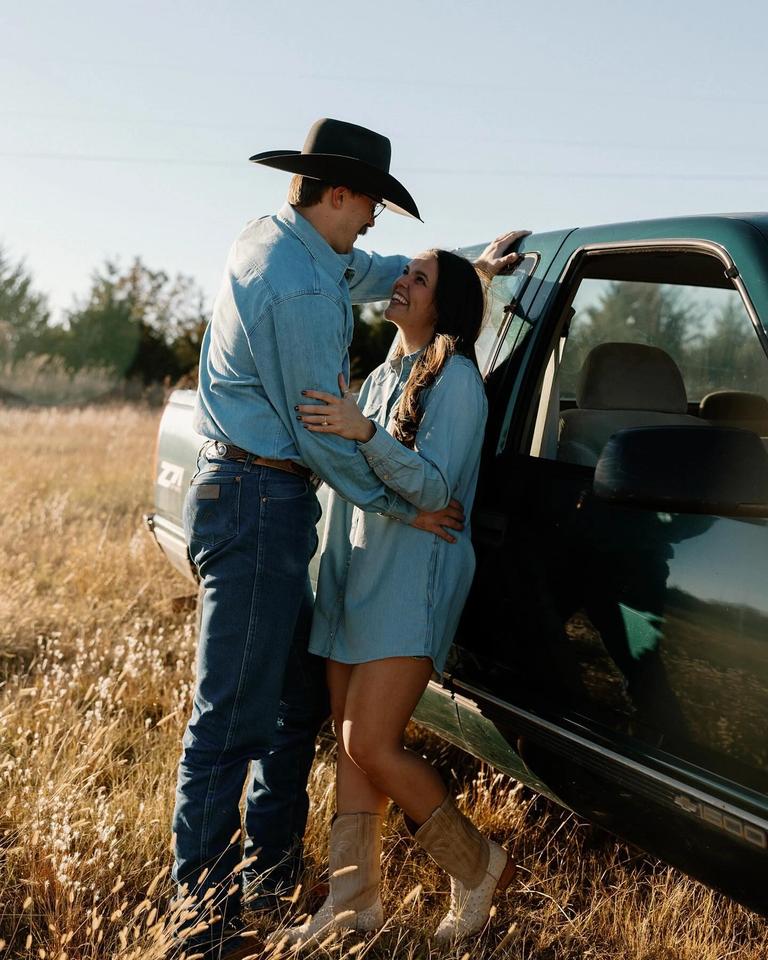 Couple standing against a car in a field wearing denim outfits