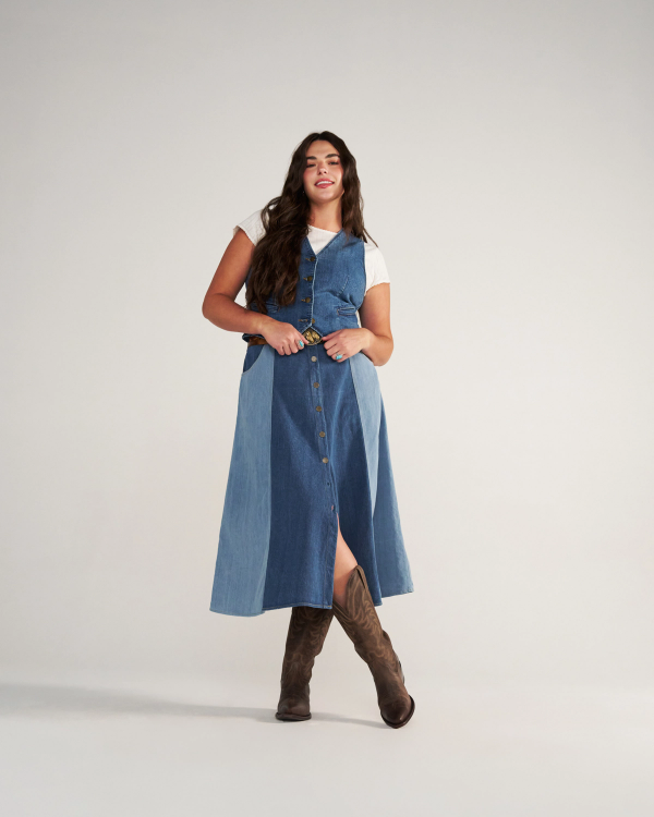 The Annie Wide Calf in Cafe Goat. A woman stands in a studio wearing The Annie Wide Calf Goat denim button-front dress over a white t-shirt, a belt, and brown cowboy boots.