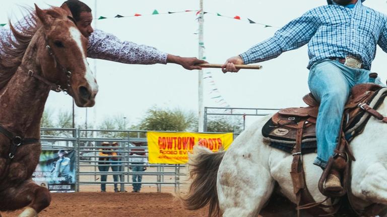 Image of cowboys riding horses at a rodeo.