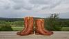 Pair of cowboy boots next to pair of roper boots against a cloudy sky