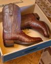 A pair of brown ostrich leather cowboy boots in an open shoebox on a patterned rug.
