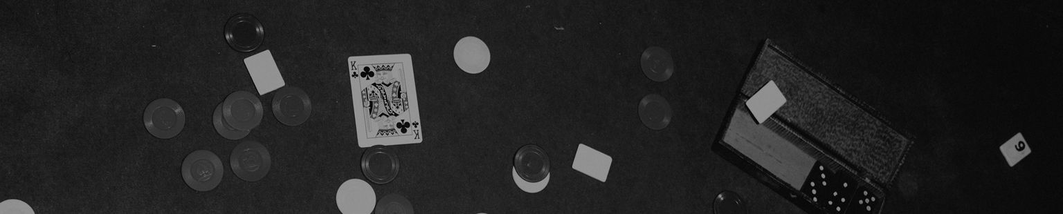 A playing card, poker chips, dice, and small rectangular slips are scattered on a dark surface.