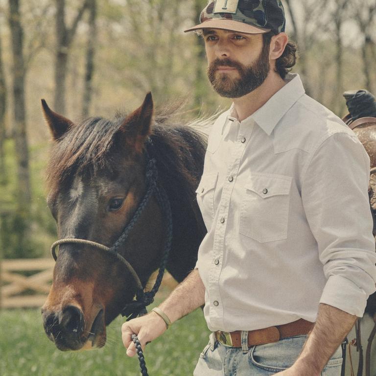 thomas rhett, country singer, wearing a tecovas hat and button down walking a horse