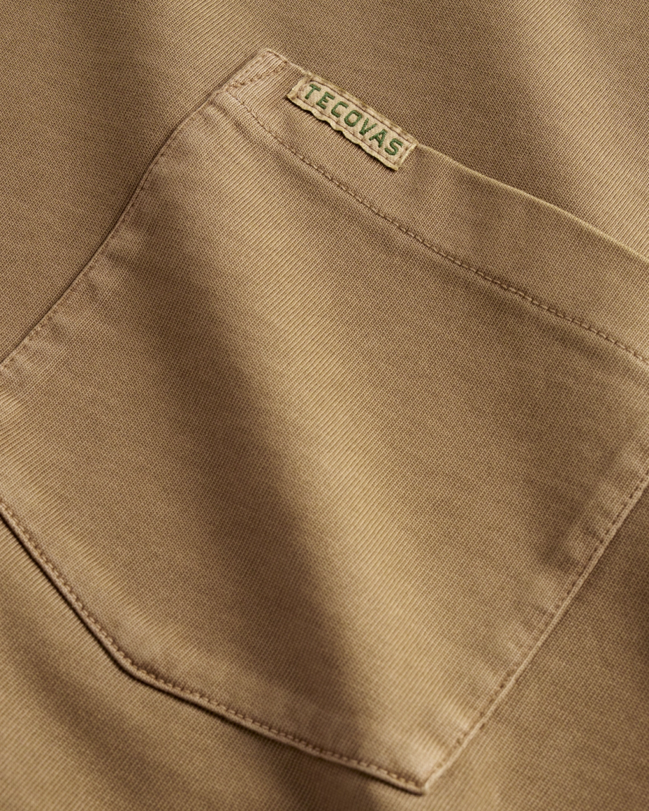 Close-up of a tan fabric shirt pocket with visible stitching, featuring a small rectangular label that reads “TECOVAS” sewn near the top edge.