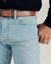 A person wearing light blue jeans, a brown leather belt, and a black long-sleeve shirt. Only the waist and right hand are visible.