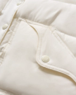 Close-up of a quilted white jacket showing a snap button closure on a slanted flap pocket and part of the buttoned front placket.