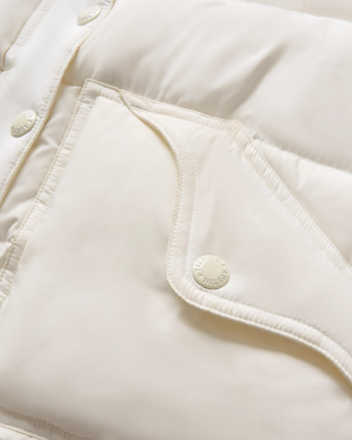 Close-up of a quilted white jacket showing a snap button closure on a slanted flap pocket and part of the buttoned front placket.
