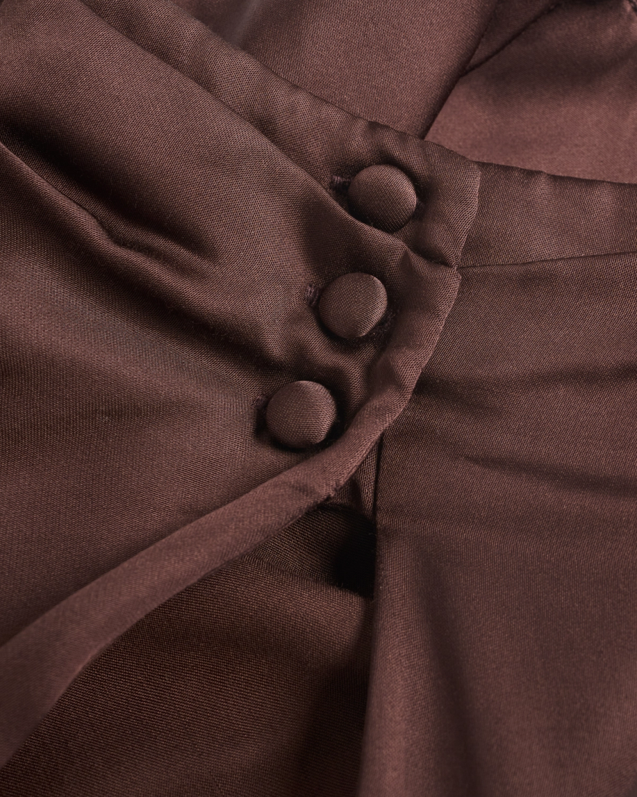 Close-up of brown fabric with three fabric-covered buttons arranged in a vertical line along a folded seam.