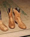 Two pairs of cowboy boots, one tan and one brown with black tops, sit on a worn wooden floor.