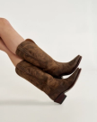 A pair of crossed legs wearing brown leather cowboy boots against a plain light background.